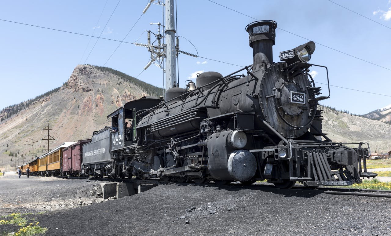 Historic steam locomotive 482 on coal tracks with passenger cars in a mountainous Colorado landscape, D&SNG or Cumbres & Toltec railway.